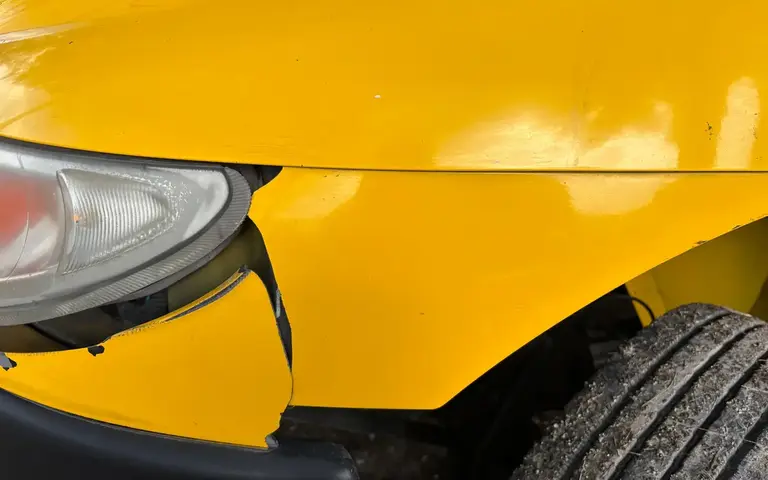 Aile avant jaune déchirée près du phare après un choc