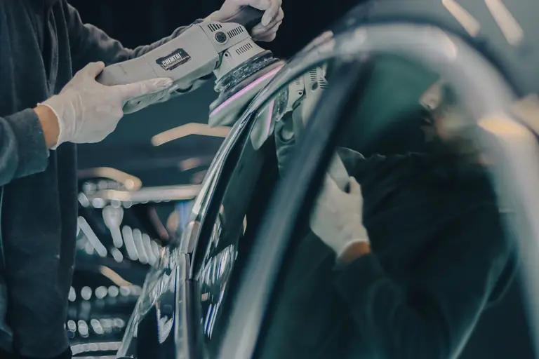 Carrossier lustrant la carrosserie sombre d'un véhicule en atelier